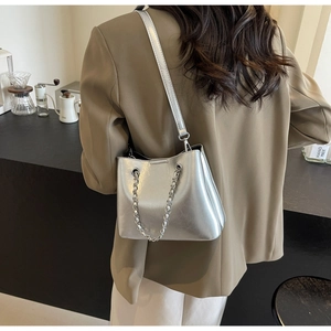 Detail der silbernen Metallic-Beuteltasche mit Kette, getragen von einem Model im Café