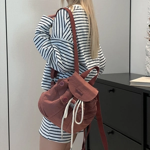 Close-up of brick red nylon backpack featuring white drawstring and decorative buttons