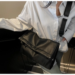 Close-up of black pebbled leather crossbody bag featuring wide strap and metal rivets