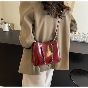 Modell mit glänzend roter Beuteltasche und Silberkette in einem modernen Café-Ambiente
