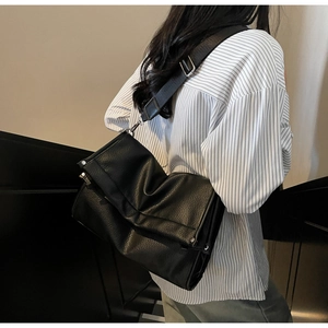 Detail of black pebbled leather tote bag showing soft texture and wide fabric strap