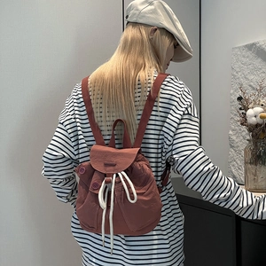 Pink nylon backpack detail showing drawstring closure and side button texture on model
