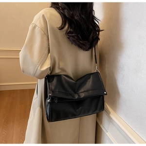 Detailed view of black pebbled leather tote bag worn with a classic camel trench coat