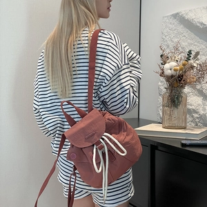 Detail of brick red nylon backpack with white drawstring closure shown on model