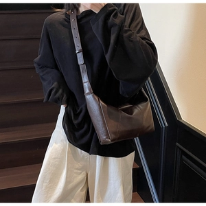 Detail of dark brown leather crossbody bag featuring adjustable wide strap and stitching