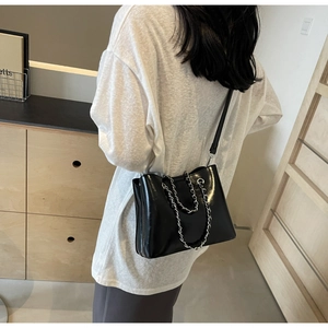 Detail einer glänzenden schwarzen Eimertasche mit Silberkette an einem Model