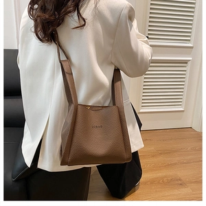 Brown lychee leather tote bag with wide strap worn by a model in a white blazer