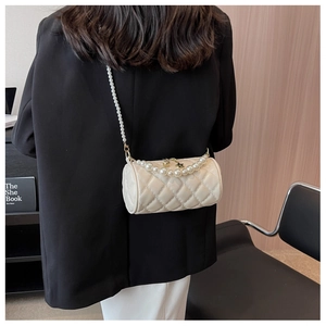 Quilted cylindrical crossbody bag with elegant pearl chain strap worn on black blazer