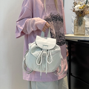 Detail of minimalist cream nylon backpack showing drawstring closure and side zipper pocket