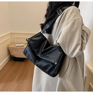 Detail view of black lychee grain leather crossbody bag with wide shoulder strap