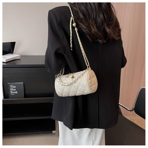 Detail of beige quilted cylinder bag with pearl handle and chain strap on a model