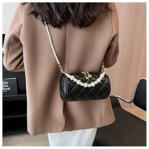 Side view of a black quilted cylinder bag with pearl strap worn by a model in a suit