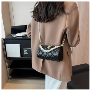 Detail view of a black quilted cylinder bag with pearl strap worn by a model