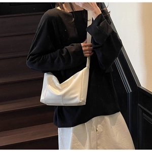 Minimalist beige leather dumpling bag with stitching details worn by model on stairs