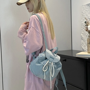 Detail view of light blue nylon backpack with drawstring closure and flap on model