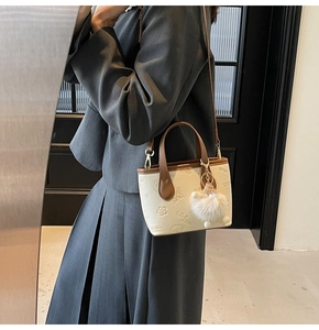Detail of cream leather bucket bag with brown handles and embossed floral patterns