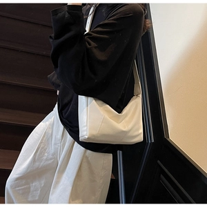 Detail of creamy white dumpling bag with vertical stitching and adjustable strap on a model