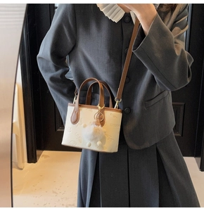 Detailed view of beige embossed mini tote bag with brown handles and white pompom charm