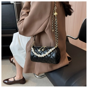 Detail of black quilted cylindrical crossbody bag with pearl handle and golden chain