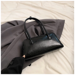 Close-up of black glossy wrinkled texture and shoulder straps on a baguette bag