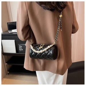 Detail of black quilted cylinder bag with large pearl handle and gold chain strap