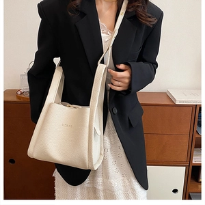 Chic cream leather bucket bag with UZBAG logo worn with a black blazer and lace dress