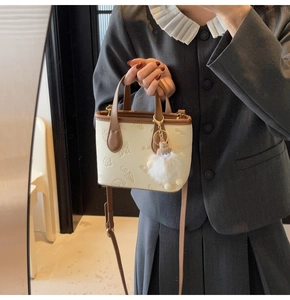 Detailed side view of mini bucket bag featuring embossed cartoon motifs and plush ball charm