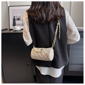 Detail of cream quilted cylinder bag with pearl strap and gold chain on shoulder