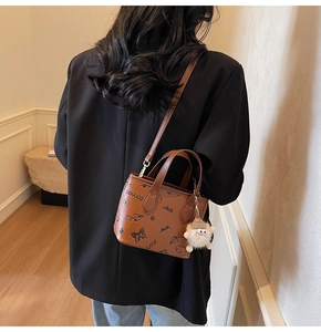 Close-up of brown leather bucket bag with cartoon prints and a plush sheep pendant