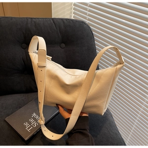 Detail of a creamy white leather hobo bag with adjustable strap on a corduroy sofa