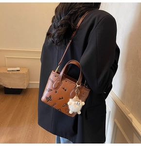 Detail of brown patterned bucket bag with cartoon prints and plush white ball pendant