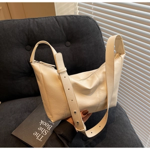 Detail of a beige leather crossbody bag featuring soft texture and silver hardware on a sofa