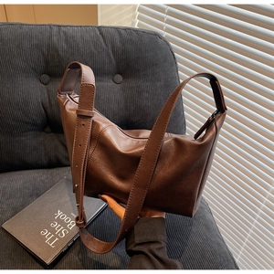 Detail of a brown leather crossbody bag featuring adjustable wide straps and zip closure