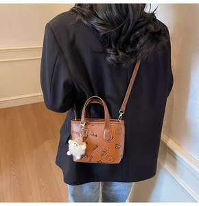 Detailed view of the brown leather mini bucket bag with cartoon prints and plush sheep charm