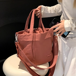 Detail of terracotta nylon crossbody bag featuring drawstring closure and textured finish