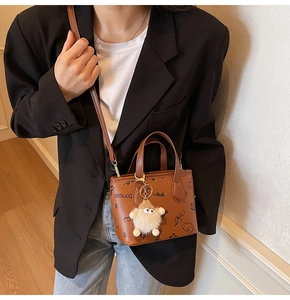 Brown crossbody bucket bag with graffiti prints and a cute plush toy pendant detail