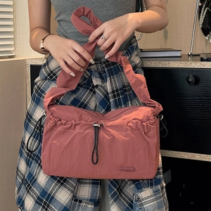 Detail of dusty pink nylon shoulder bag showing pleated texture and wide strap on model
