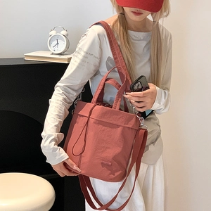 Detail of drawstring nylon crossbody bag in brick red showing texture and strap