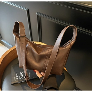 Detailed view of dark brown matte leather shoulder bag with adjustable strap on a chair