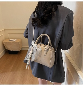 Detail of beige mini bowling bag with lace bow and scarf on a female model