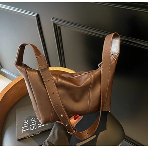 Detail of a dark brown leather dumpling bag with vertical stitching on a wooden chair