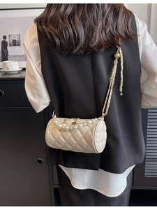 Chic beige quilted cylinder crossbody bag with pearl chain shown on a model's shoulder