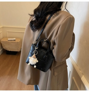 Detail of black embossed bucket bag with plush charm on brown blazer street style