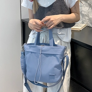 Detail of light blue nylon crossbody bag featuring white drawstring closure and top handle