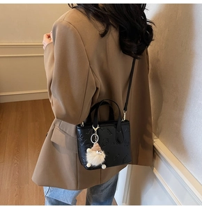 Detail view of black embossed bucket bag with plush charm on elegant model in studio