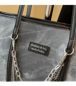 Détail d'un sac cabas en denim gris avec étiquette en cuir noir et chaînes argentées