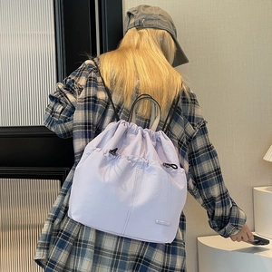 Detail view of a light purple drawstring backpack worn by a model in a minimalist room