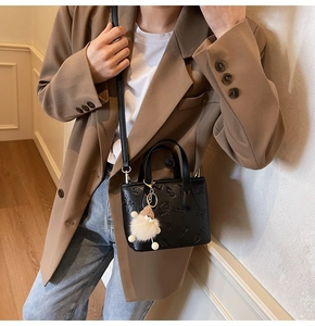 Detail of black mini crossbody bucket bag with embossed patterns and plush charm on model