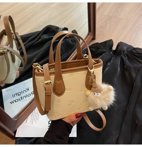Detail of cream crossbody bag with embossed patterns and brown leather strap and plush charm