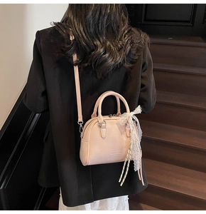 Detail of elegant peach crossbody bag with lace bow accessory and top handles